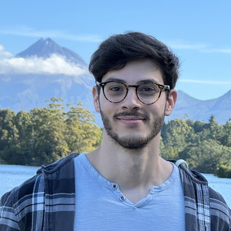 A photo of me taken in New Zealand. In the background there is a lake and Mount Taranaki.